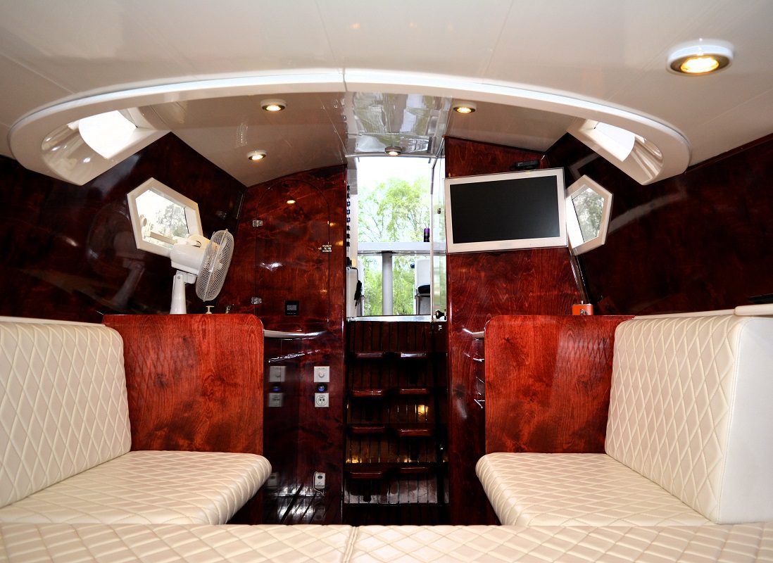 Mahogany boat cabin interior with kitchenette, flat screen TV, and comfortable leather seating