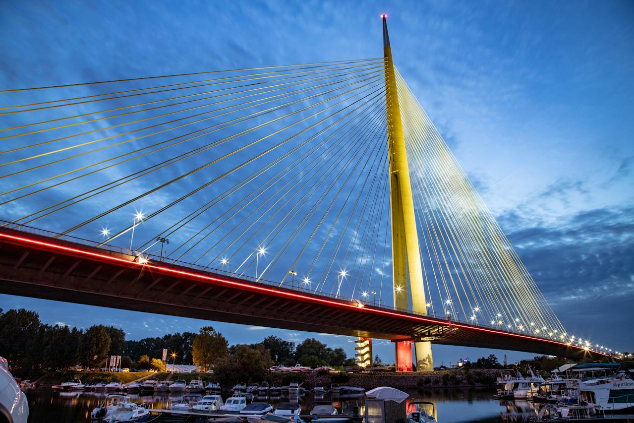 Spectacular night view of Belgrade Ada Bridge from our Belgrade River Cruise boat on the Sava River, showcasing the world's largest single-pylon cable-stayed bridge