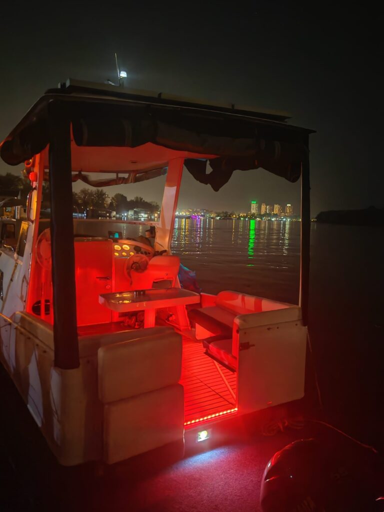 Interior of a luxury cruising boat at night with vibrant red LED lighting on the deck and Belgrade city skyline reflected in the Sava River.